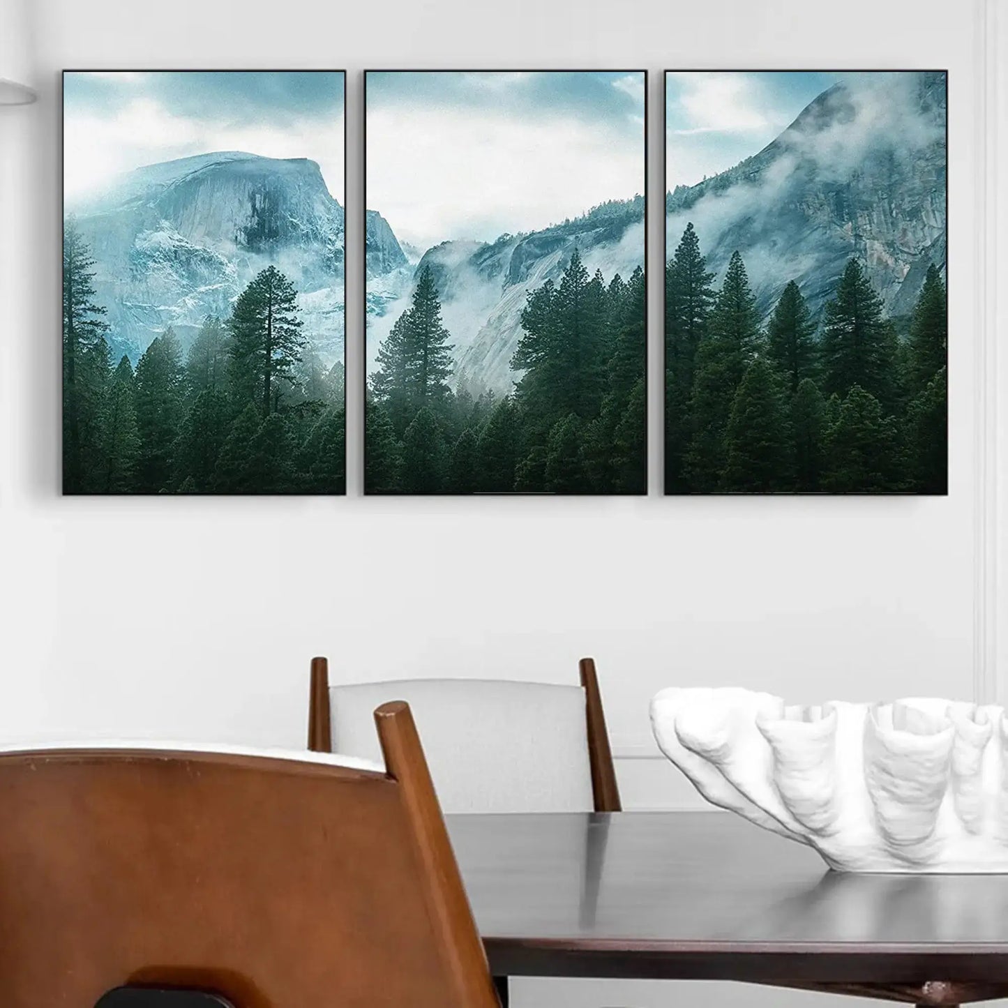 Three framed mountain landscapes above a dining table with chairs.