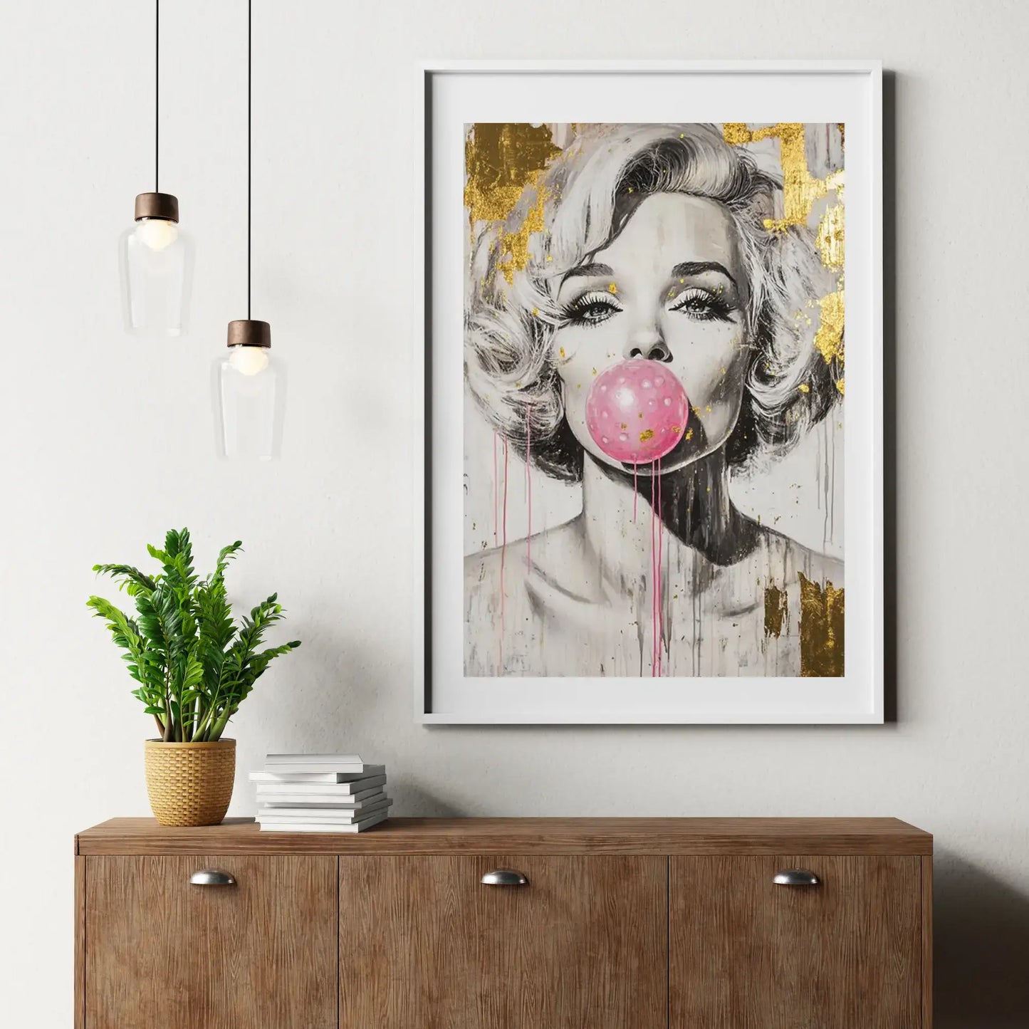 Framed artwork of a stylized portrait with a pink bubble gum on a wall above a wooden cabinet.