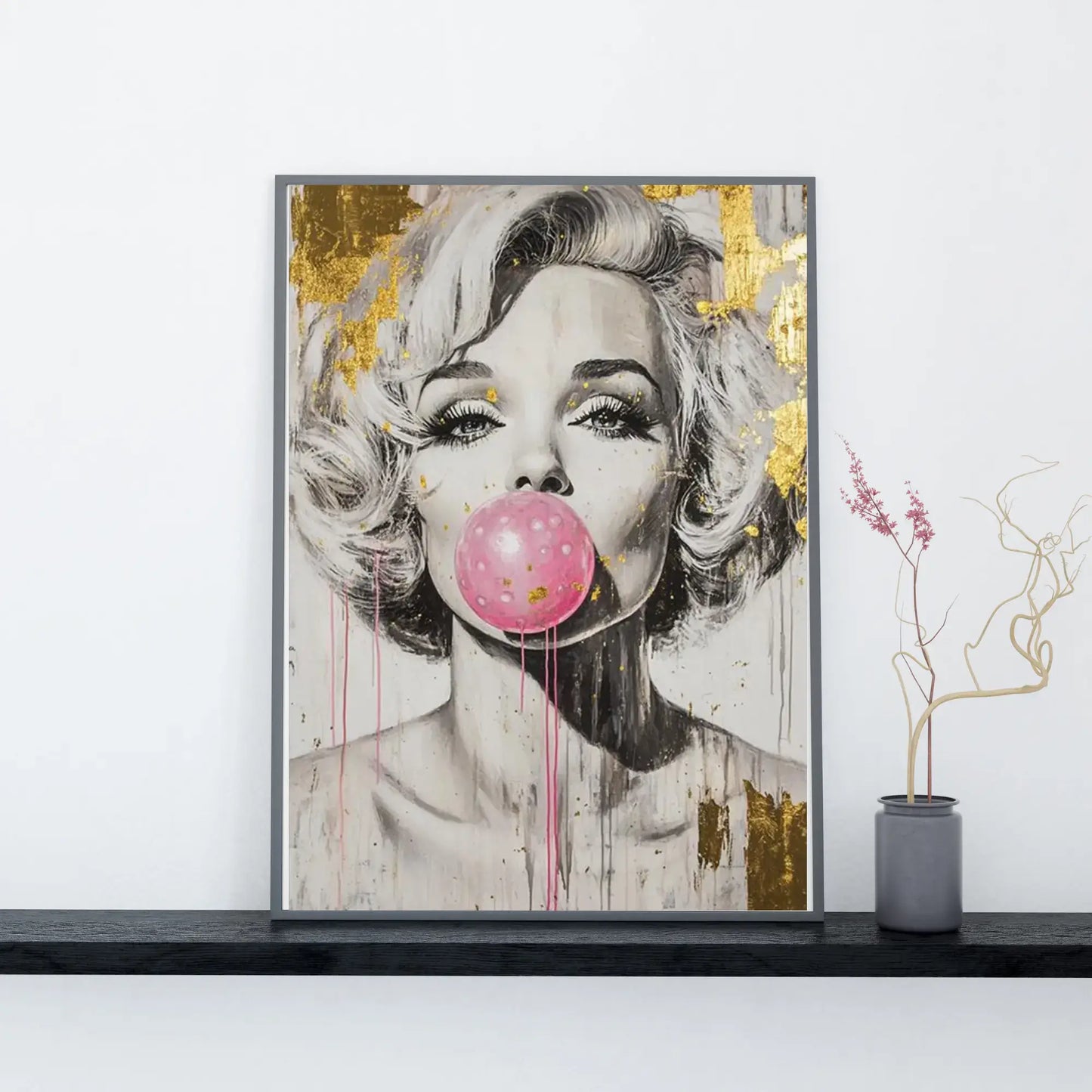 Framed artwork of a woman blowing a pink bubble with gold accents on a white wall.