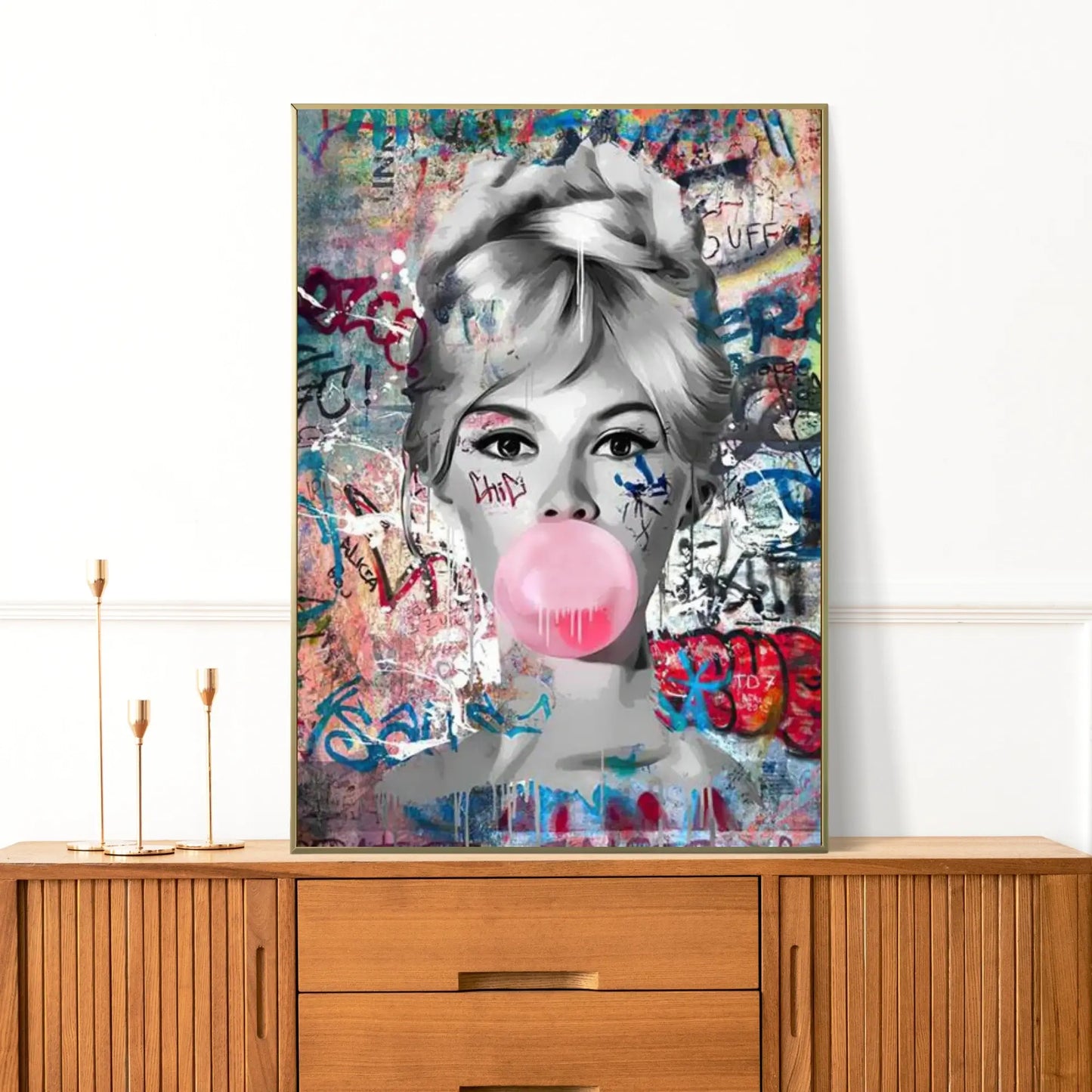 Framed artwork of a woman blowing a pink bubble gum bubble on a colorful background, displayed on a wooden cabinet.