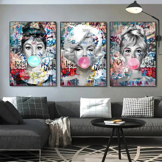 Three colorful art prints of famous faces blowing bubble gum on a wall above a sofa.